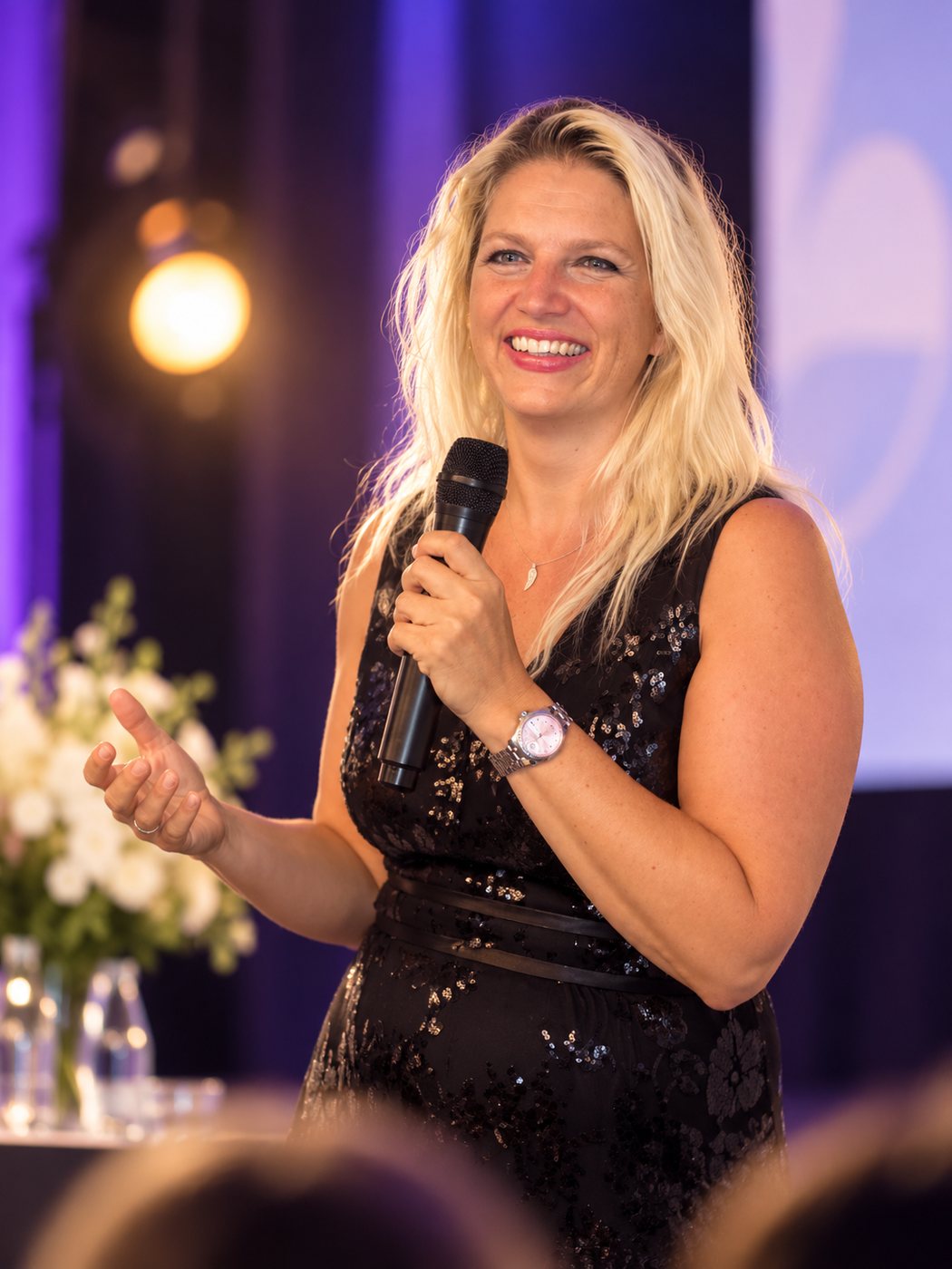 Nathalie Sameli spricht im schwarzen Paillettenblazer mit Mikrofon auf der Bühne